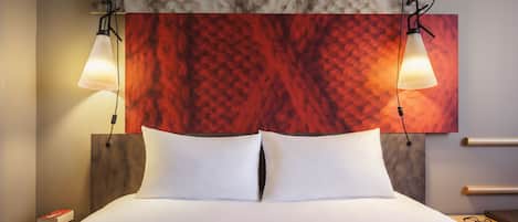 A neatly made bed with white linens and two pillows, a headboard with a red abstract design, and two pendant lights hanging above.