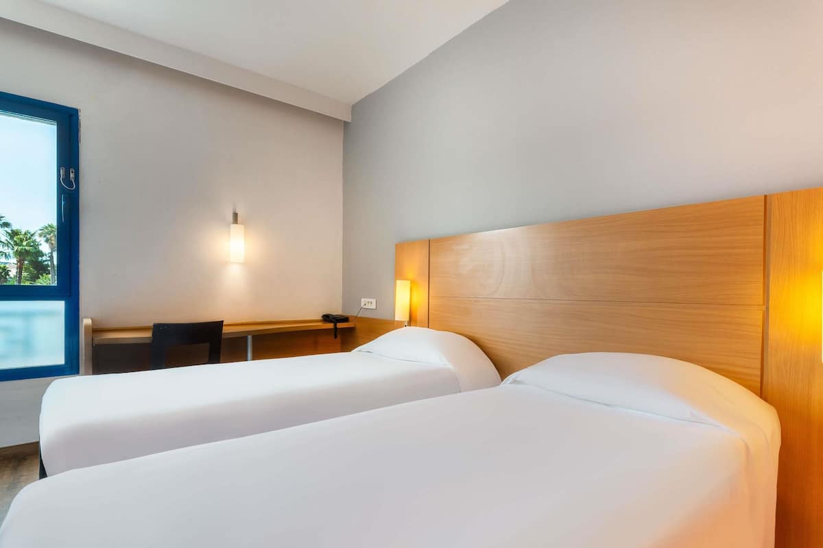 Une chambre d’hôtel avec deux lits, un bureau, une chaise, un téléphone et une fenêtre donnant sur un paysage agréable.
