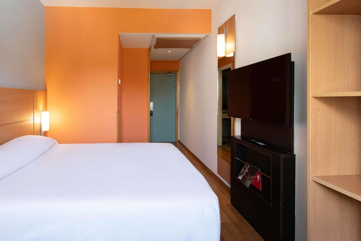 Une chambre d’hôtel avec un lit, un téléviseur posé sur un meuble en bois et une porte donnant sur une autre pièce.