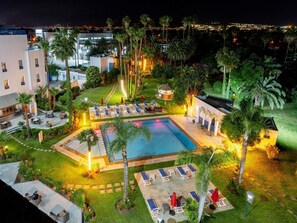 Área de piscina com espreguiçadeiras e uma piscina pequena, cercada por palmeiras e um edifício.
