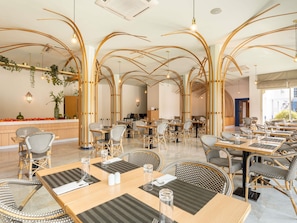 Um restaurante com arcos de madeira altos, cadeiras de vime e mesas com jogos americanos.