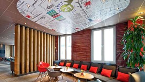 Un área de estar moderna con un muro de listones de madera, un sofá curvo con cojines rojos y una planta verde grande.