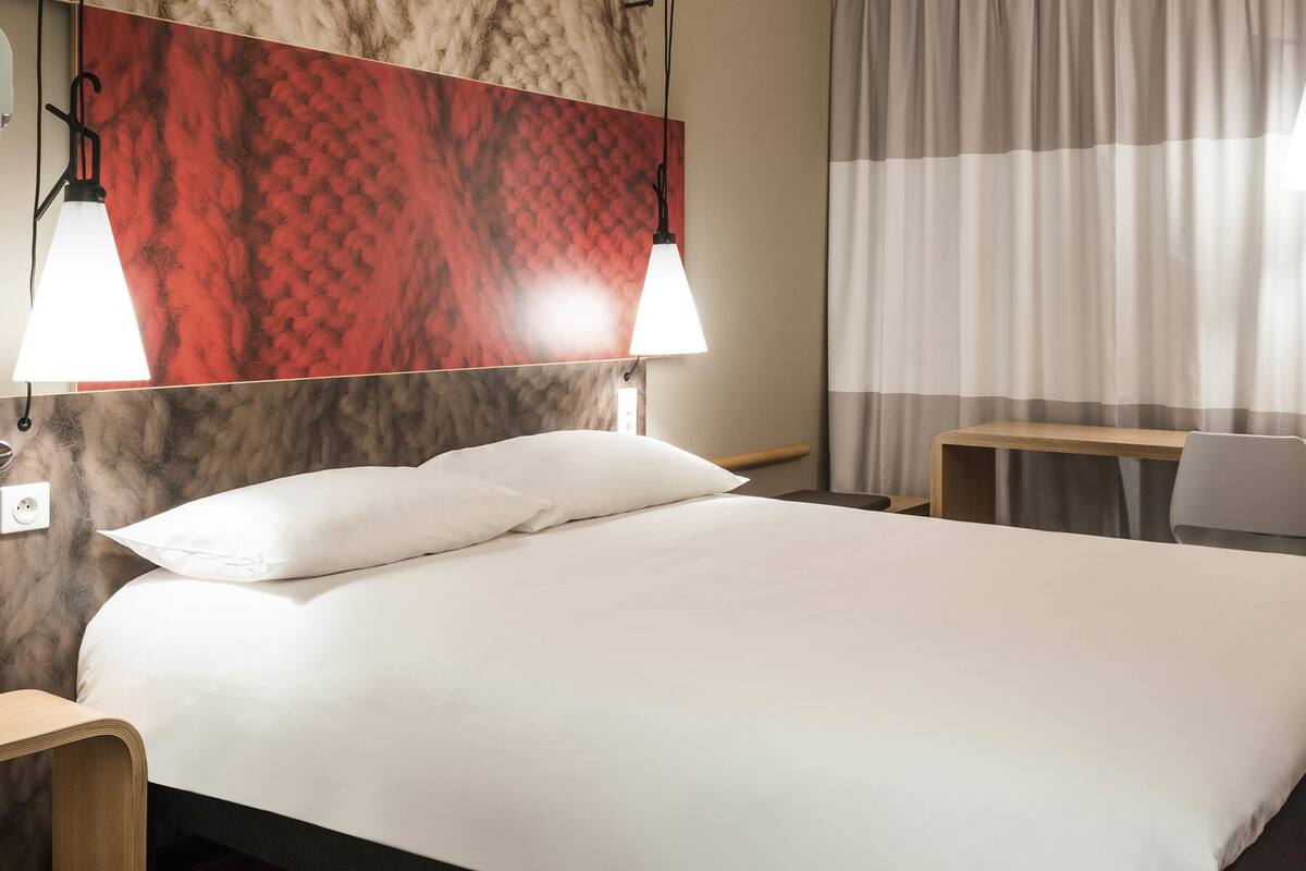 Ein Hotelzimmer mit einem Bett, zwei Nachttischlampen, einem Schreibtisch und einem Sessel.