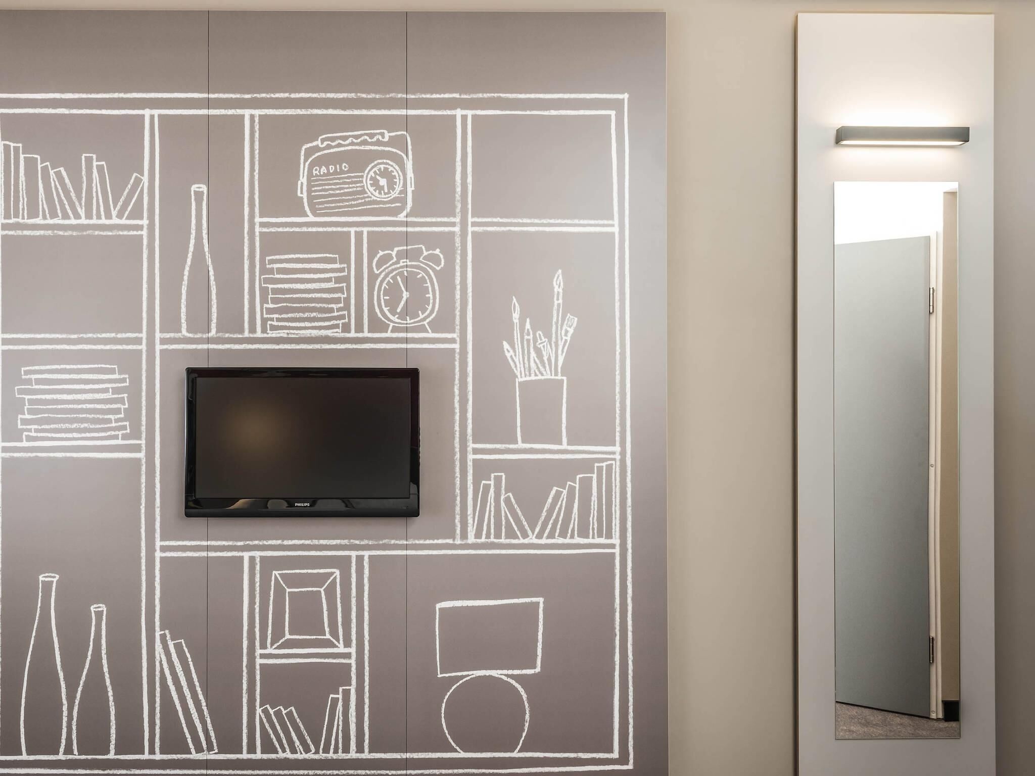 Ein modernes Zimmer mit einem Flachbildfernseher, der an einer Tafelwand angebracht ist, einem Spiegel und einer Tür.
