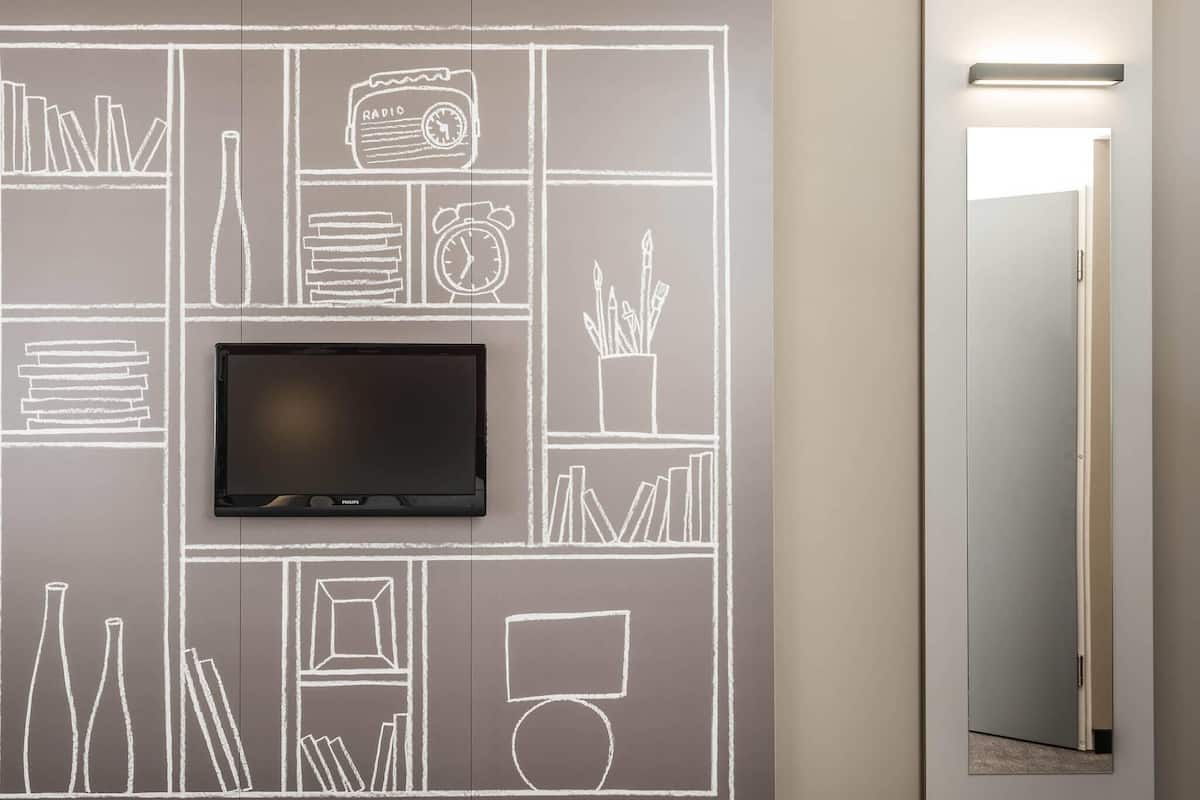 Quarto moderno com televisão de tela plana presa em uma parede de lousa, um espelho e uma porta.