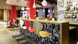Un área de bar moderna con decoración en rojo y negro, varias lámparas colgantes y una variedad de taburetes de bar.