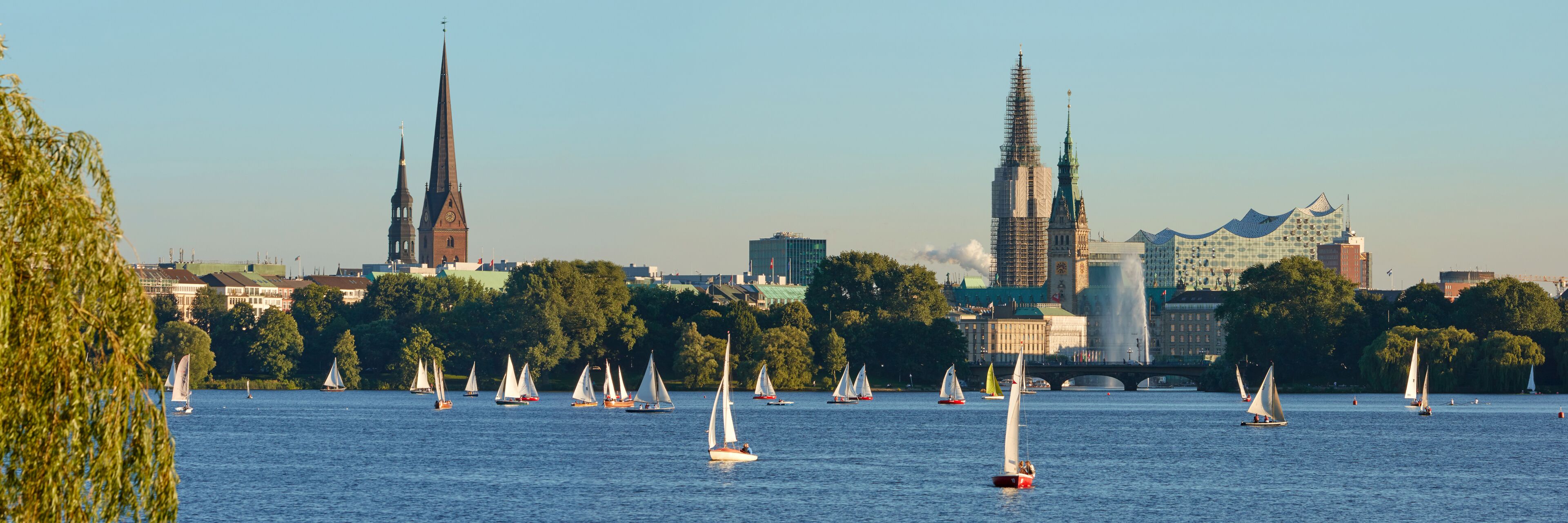A river with sailboats, a church, and a modern building with a spire.