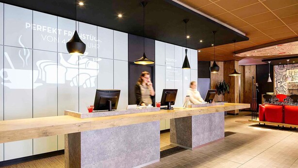 Una recepción con diseño moderno, un área de descanso con sillas rojas y una pared decorada con un diseño de taza de café y vapor.