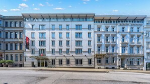 Un hotel de varios pisos con un estilo arquitectónico clásico, que presenta una entrada central con dosel, ventanas amplias y una bandera destacada.