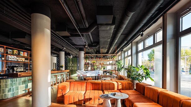 A modern bar area with orange seating, a bar counter, and large windows. - Me and All Hotel Berlin East Side, by Hyatt - NEW OPENING (Berlin)