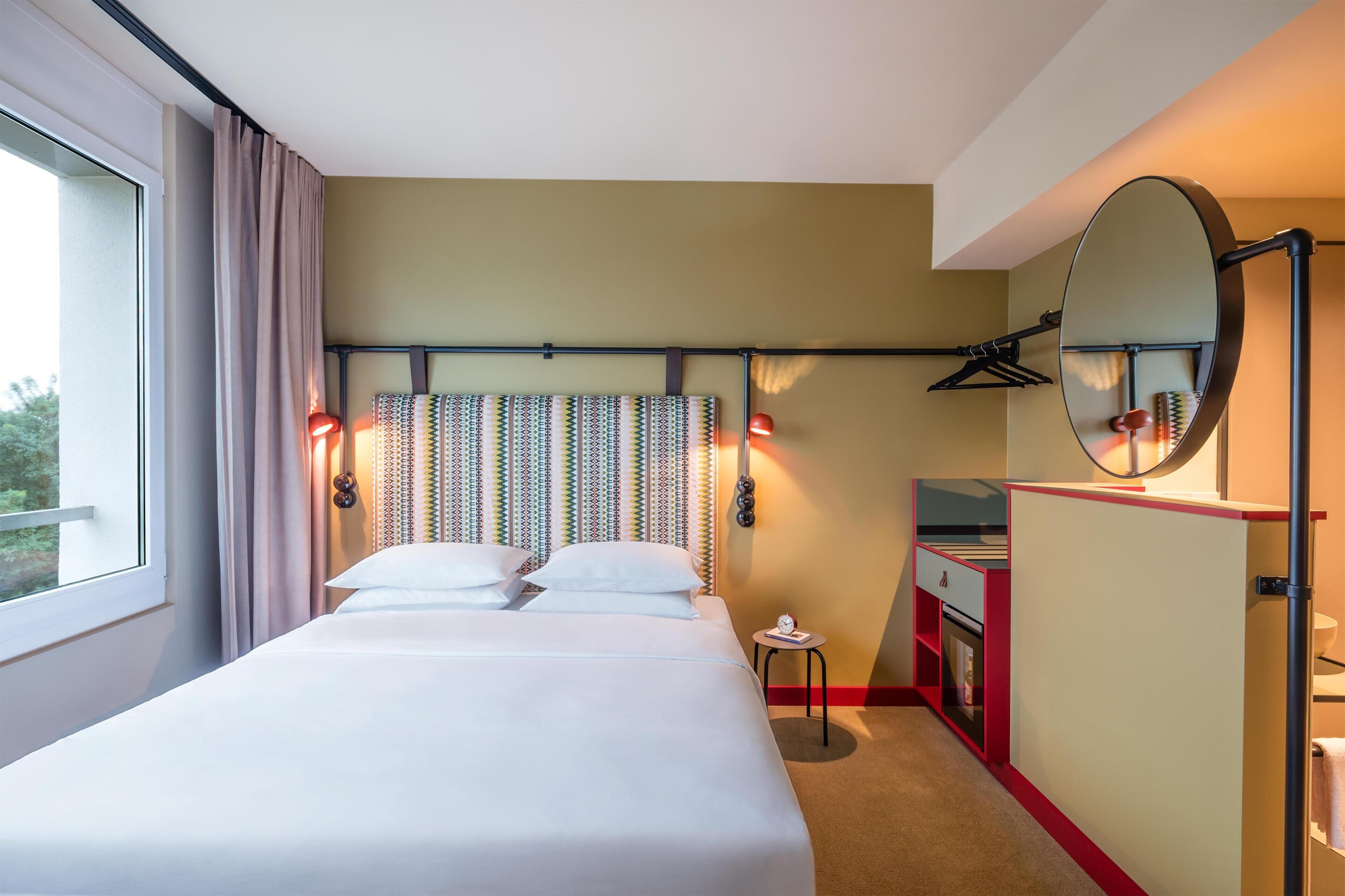 A hotel room with a large bed, a bedside table, a mirror, and a wardrobe.