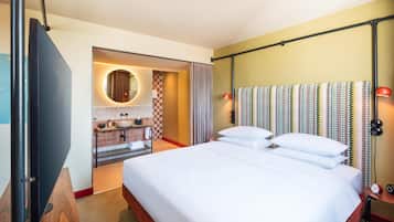 Habitación de hotel con una cama grande, un baño con lavamanos y espejo, y vista al pasillo.