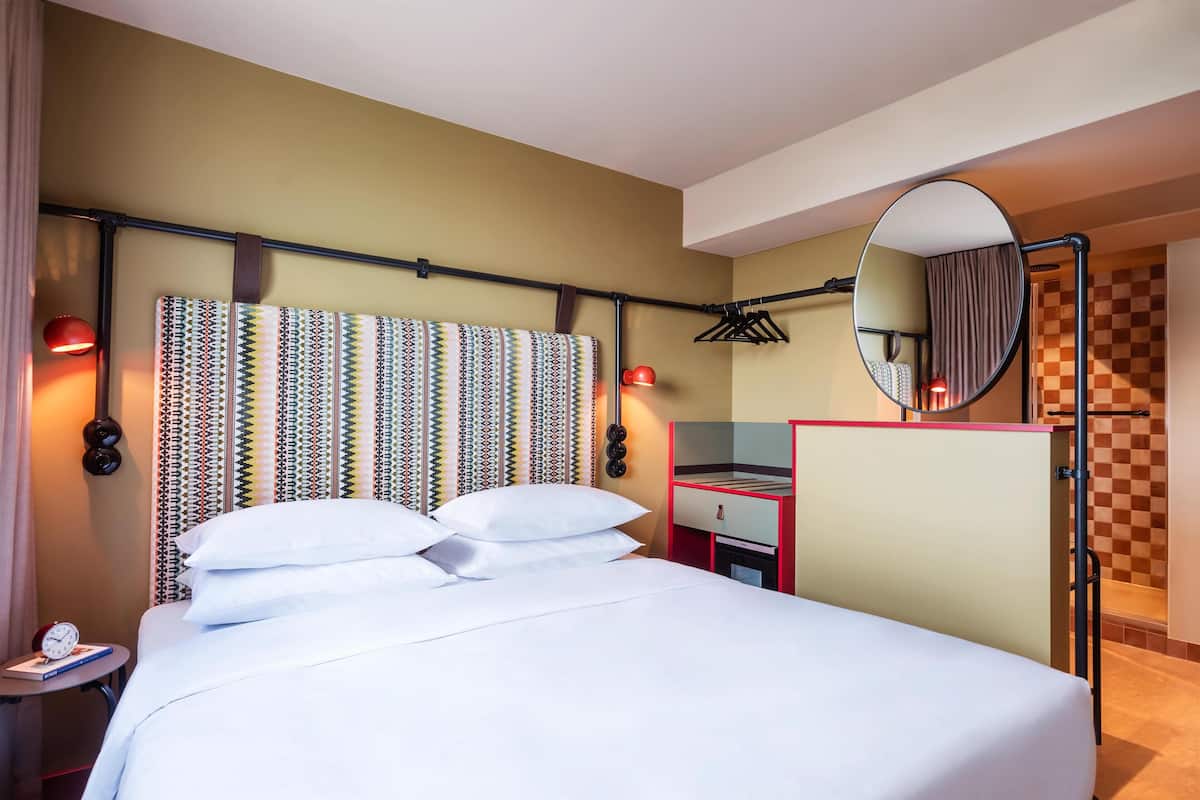 A hotel room with a bed, a bedside table with a clock, a mirror, and a checkered wall pattern.