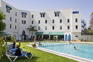 A pool area with lounge chairs, a swimming pool, and a building with multiple windows and balconies. - Hotel ibis Oujda (Oujda)