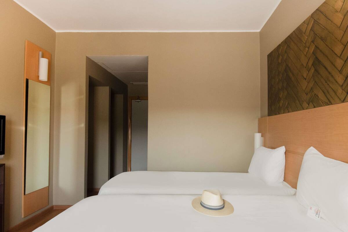 A hotel room with two beds, a television, a mirror, and a wooden accent wall.