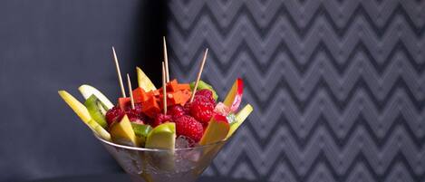 Ensalada de frutas en una copa de martini sobre una mesa, con un cojín estampado al fondo.