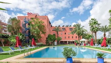 Un hotel con piscina, sombrillas rojas y palmeras.