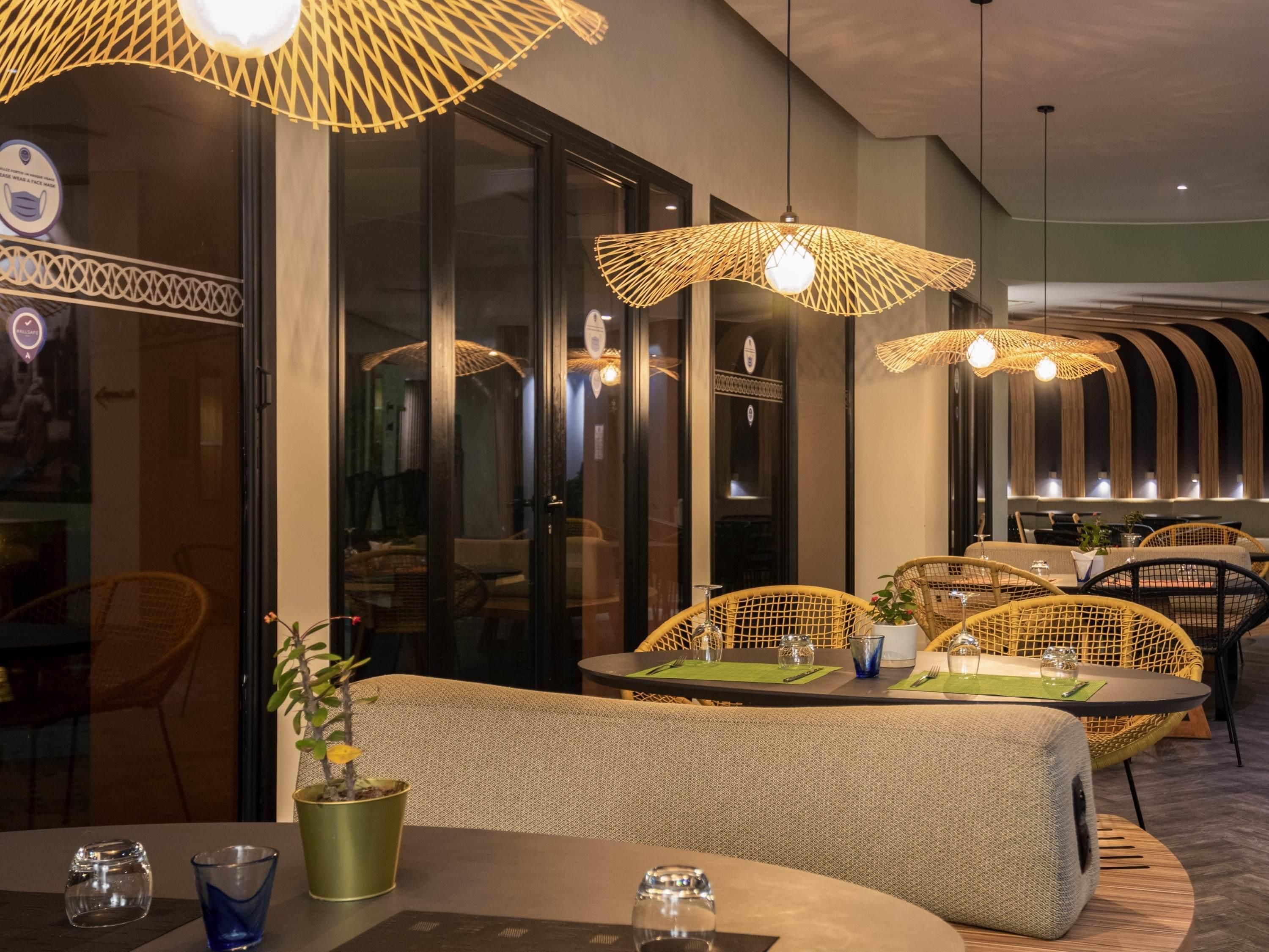A restaurant with wicker furniture, round tables, and hanging wicker lamps.