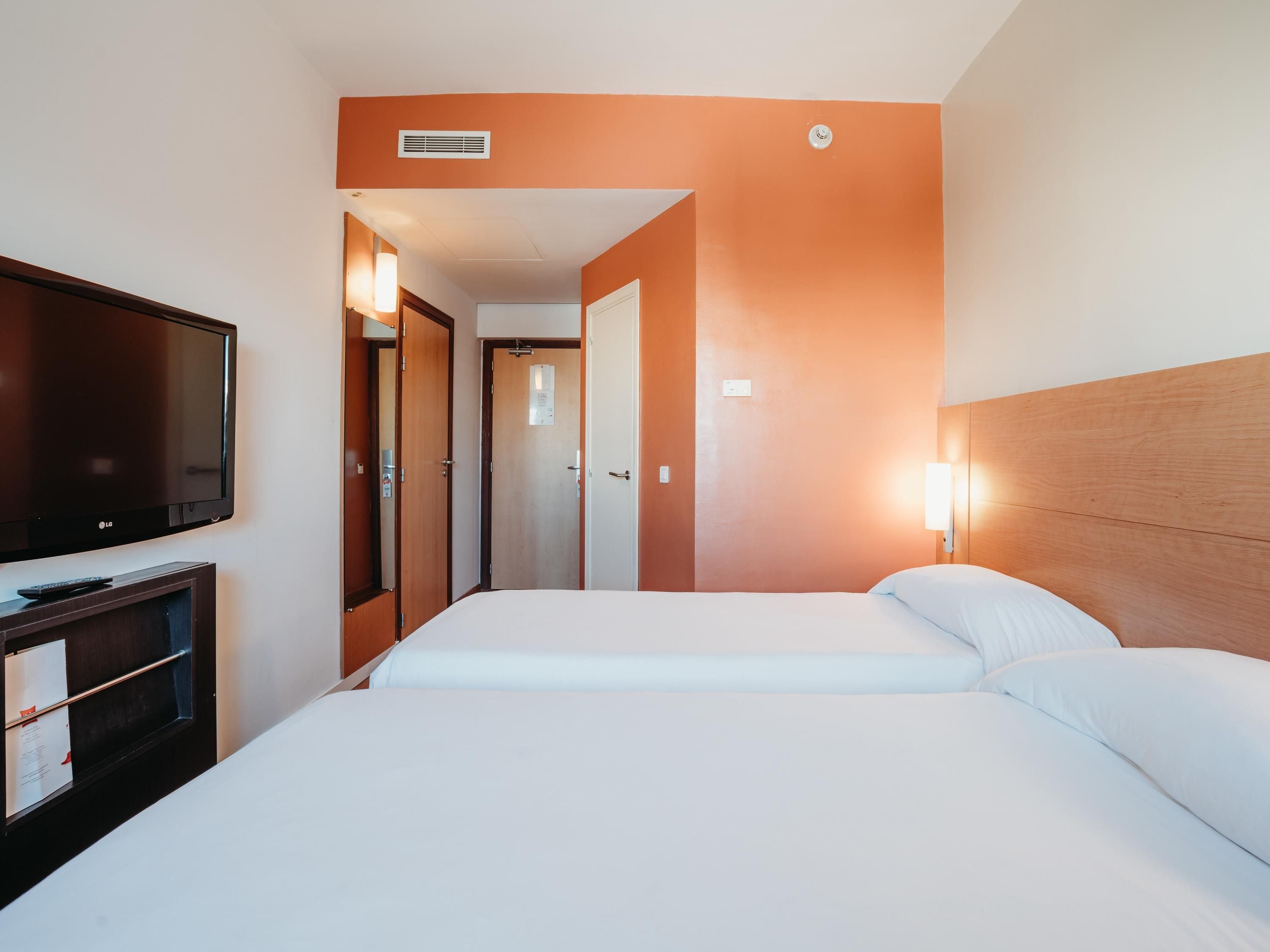 Habitación de hotel con dos camas, un televisor y un escritorio con lámpara.
