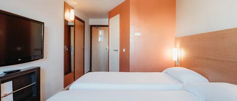 Habitación de hotel con dos camas, un televisor y un escritorio con lámpara.