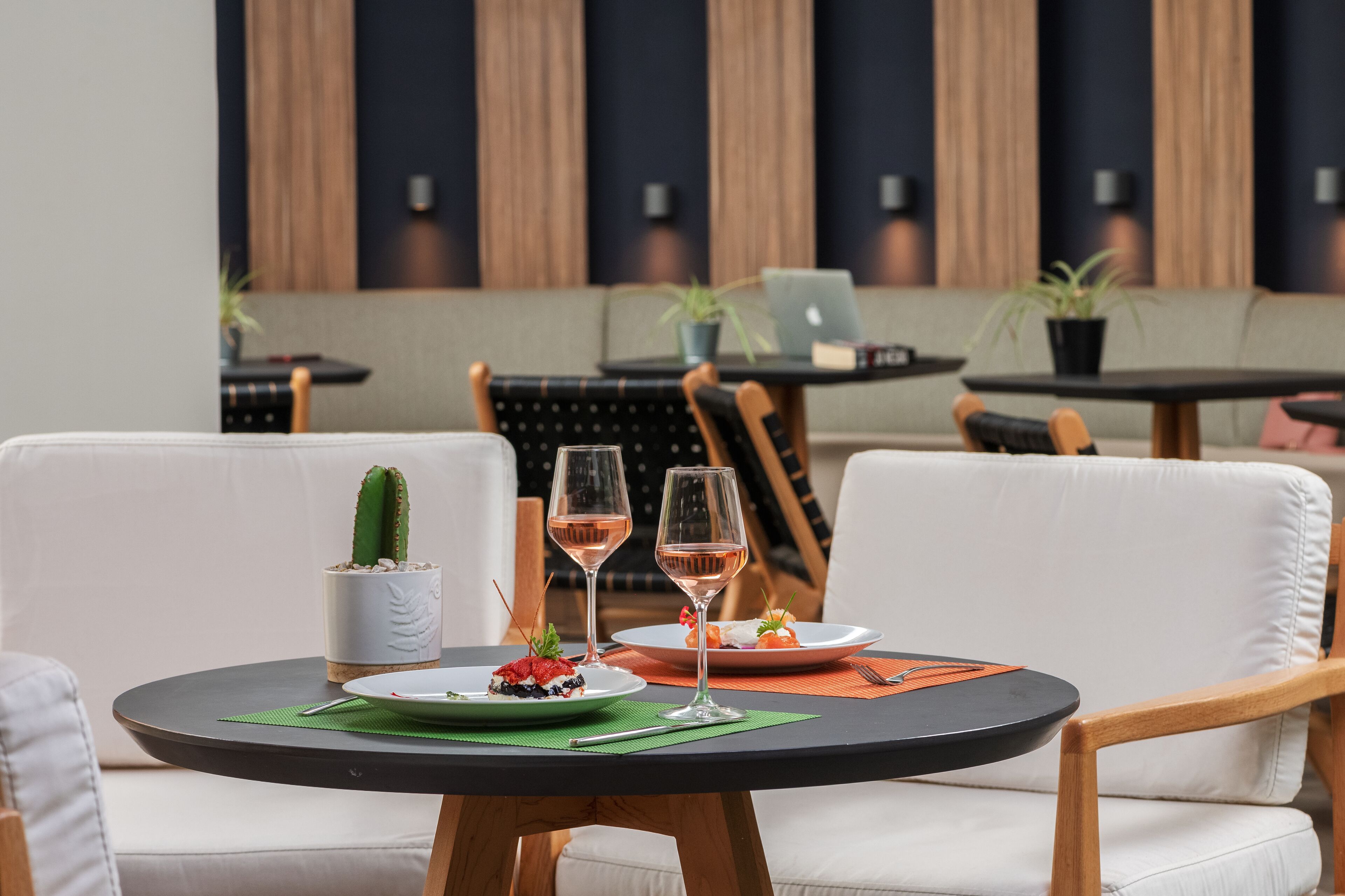 Een eethoek met een ronde tafel, twee stoelen, een cactus, twee wijnglazen en een bord met eten.