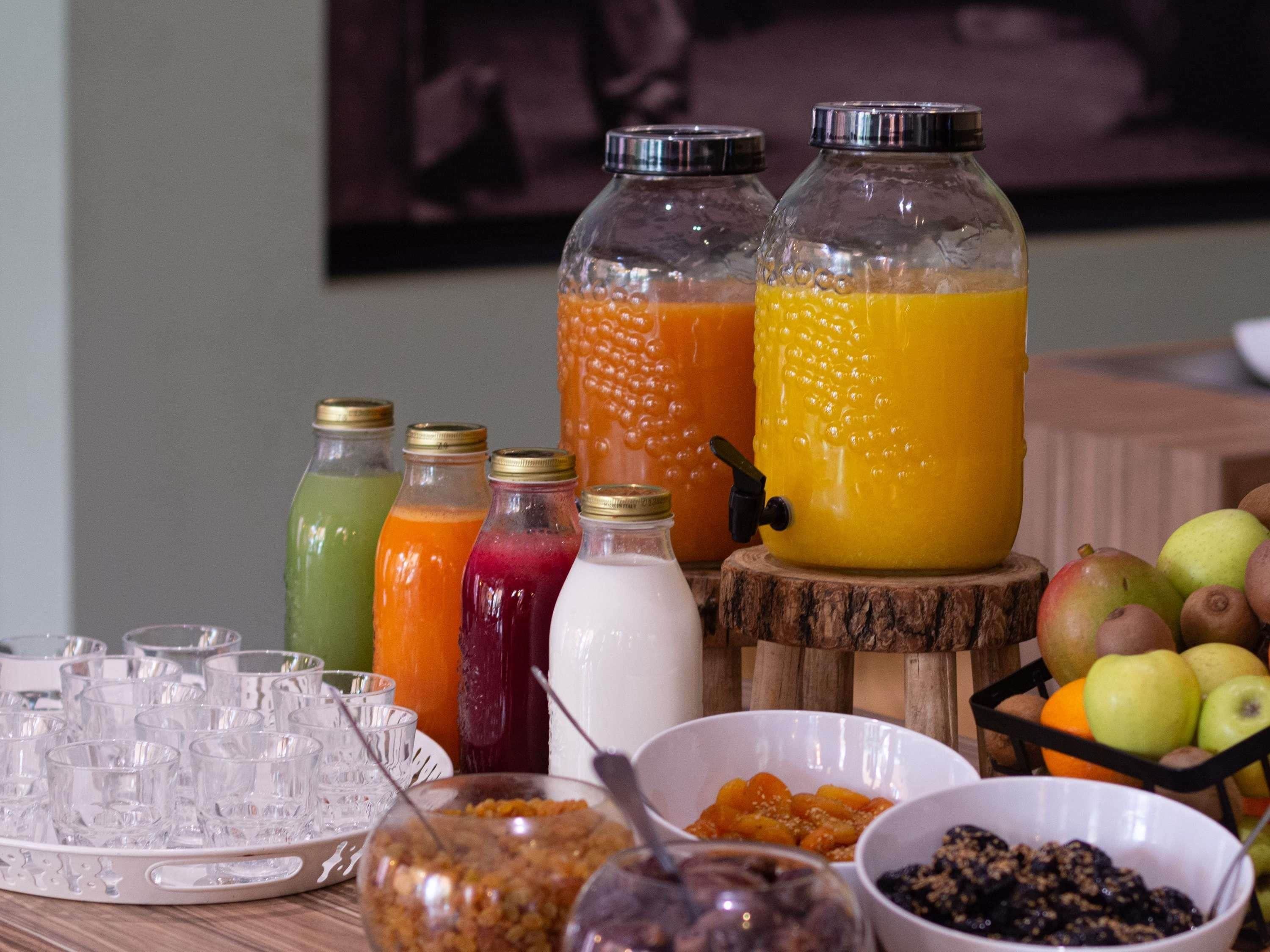 Um buffet de café da manhã com diversos sucos, uma saladeira de frutas e uma bandeja de copos.