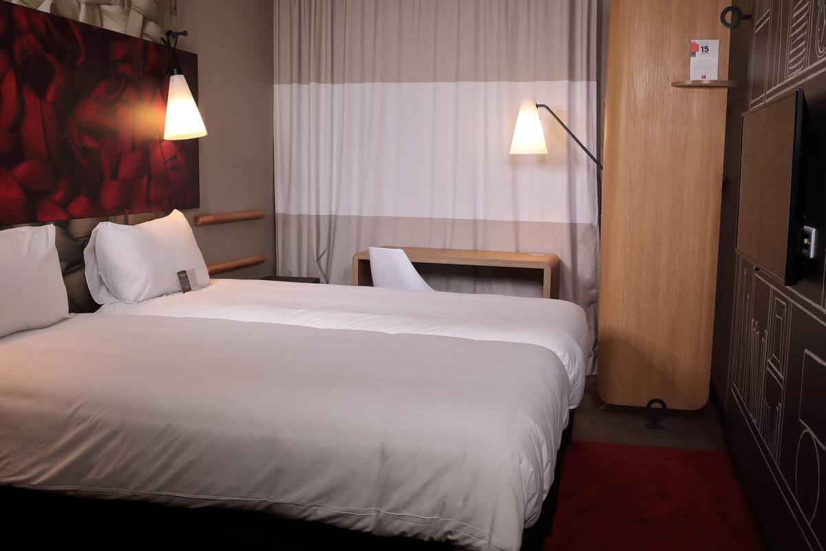 A neatly made bed with white linens, a wooden headboard, and two bedside lamps.