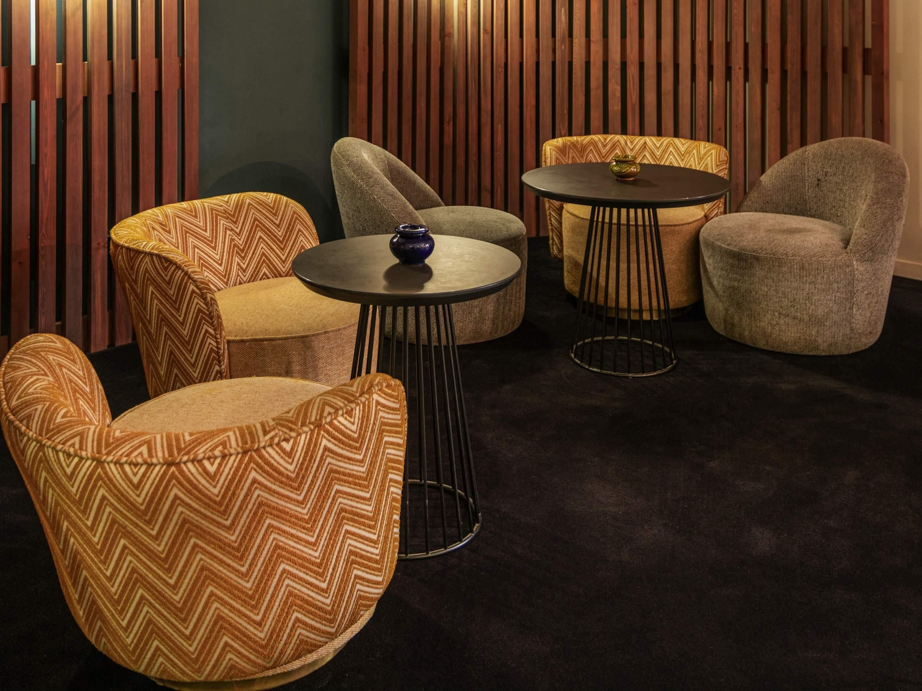 A seating area with cushioned chairs and round tables, featuring a chevron pattern upholstery and a small decorative vase on one table.