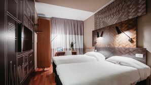Ein Hotelzimmer mit zwei Betten, einem Schreibtisch mit Computer, einem Spiegel und einer Wand mit Fischgrätmuster.