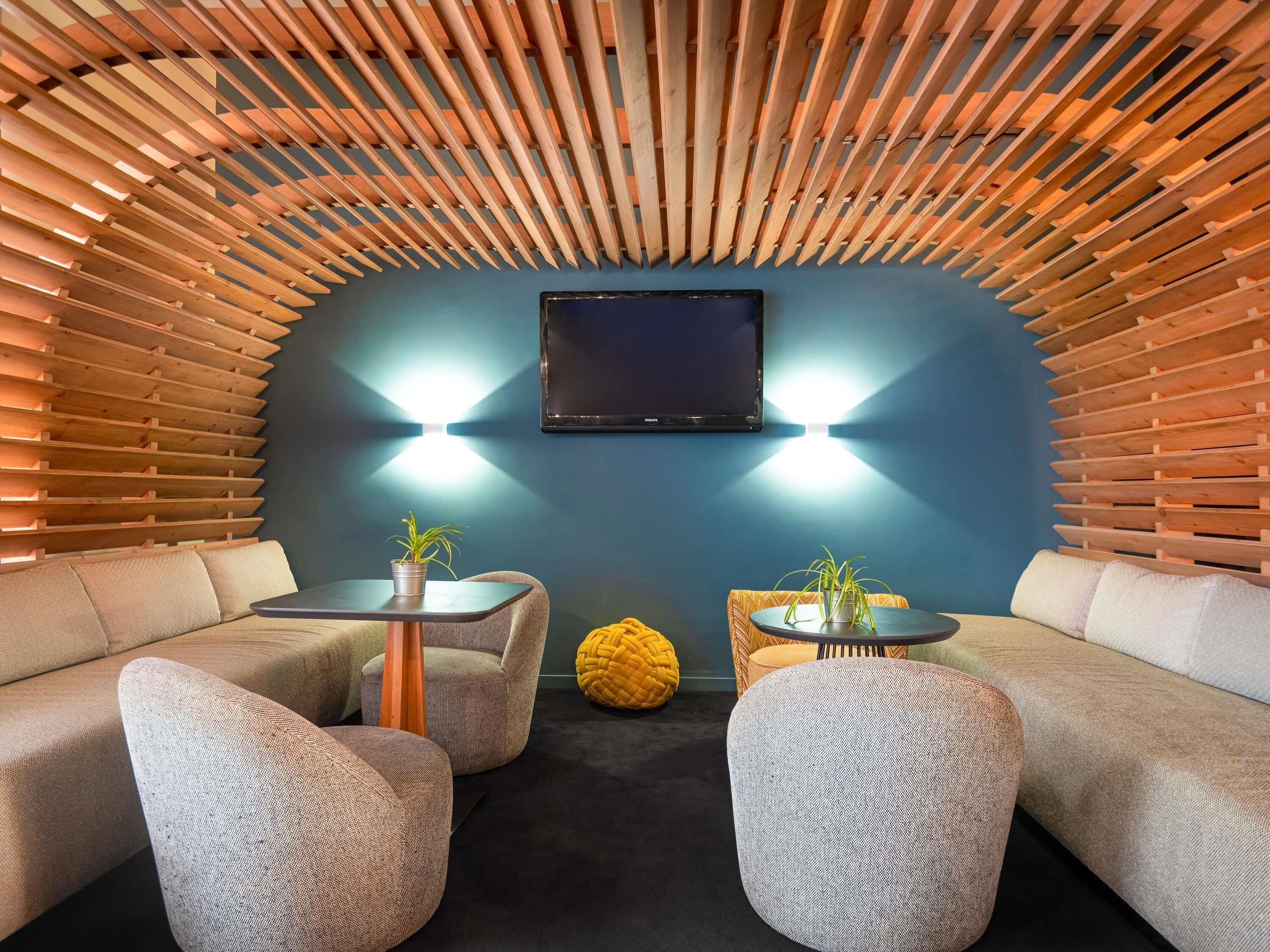 Una habitación acogedora con techo de madera curvada, un televisor de pantalla plana en la pared y dos zonas de estar con mesitas y plantas en macetas.