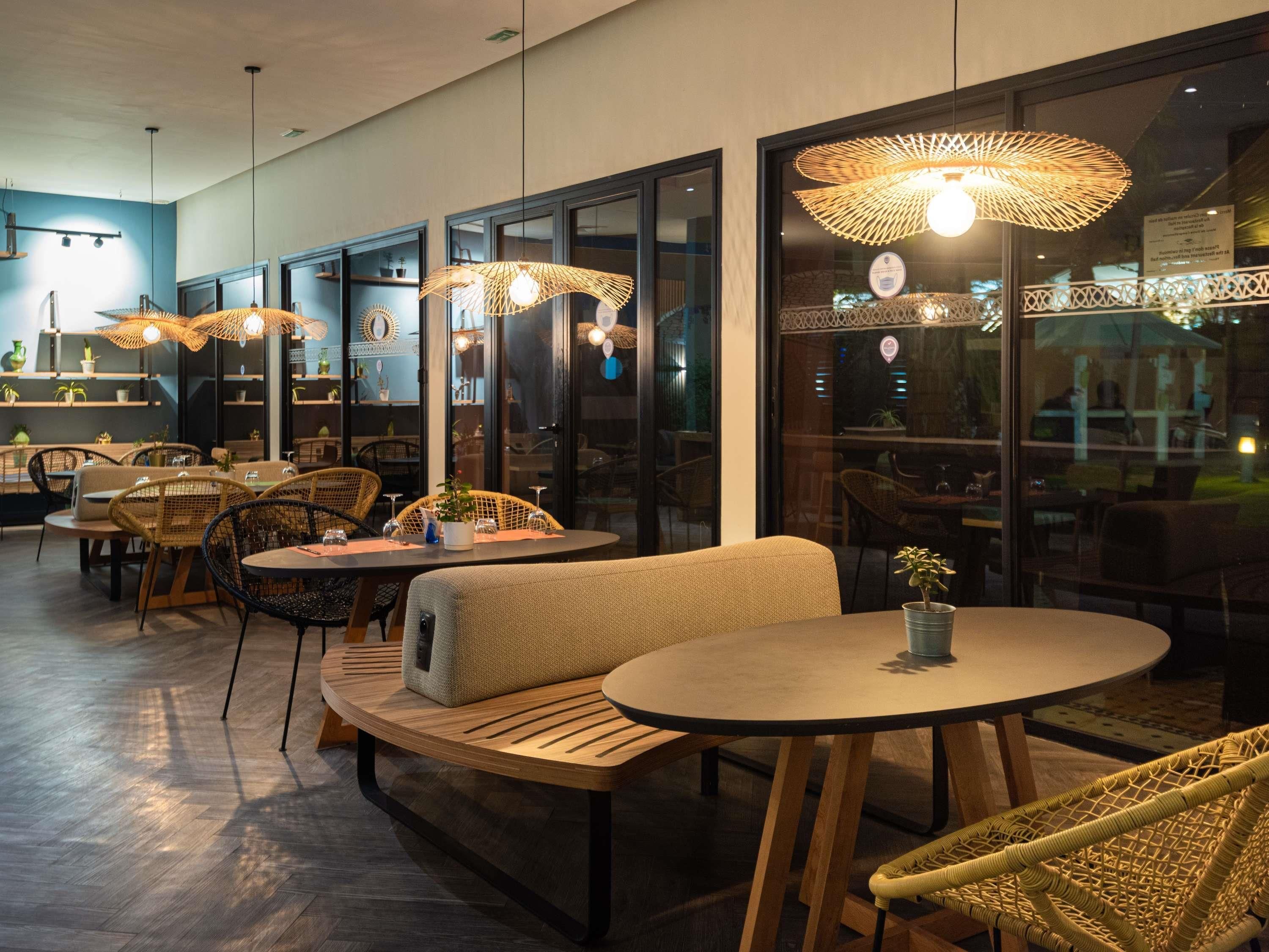 A restaurant interior with round tables, wicker chairs, and hanging lamps.