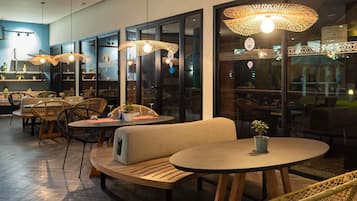 Un interior de restaurante con mesas redondas, sillas de mimbre y lámparas colgantes.