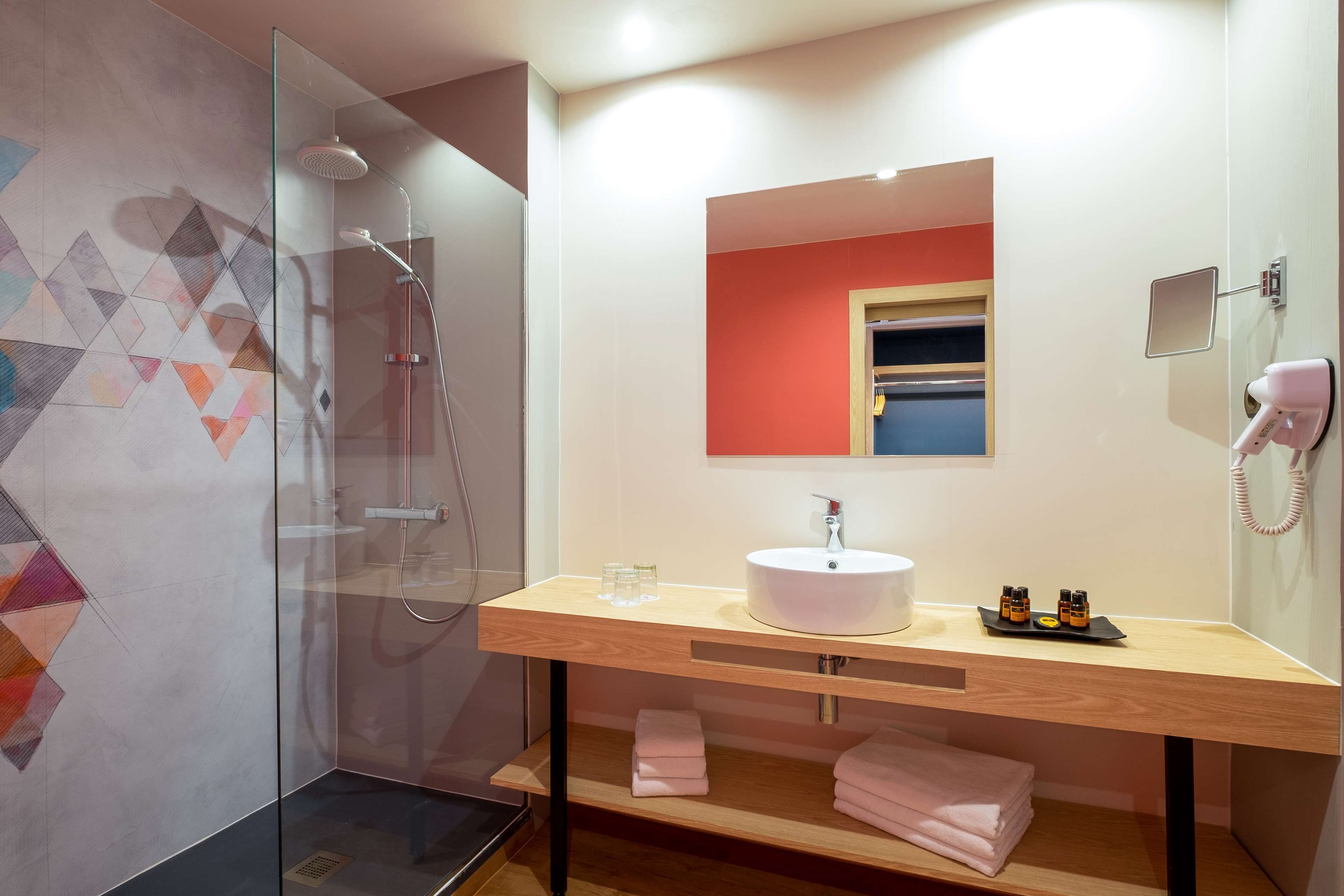 A modern bathroom with a glass-enclosed shower, a wooden vanity with a sink, and a mirror.