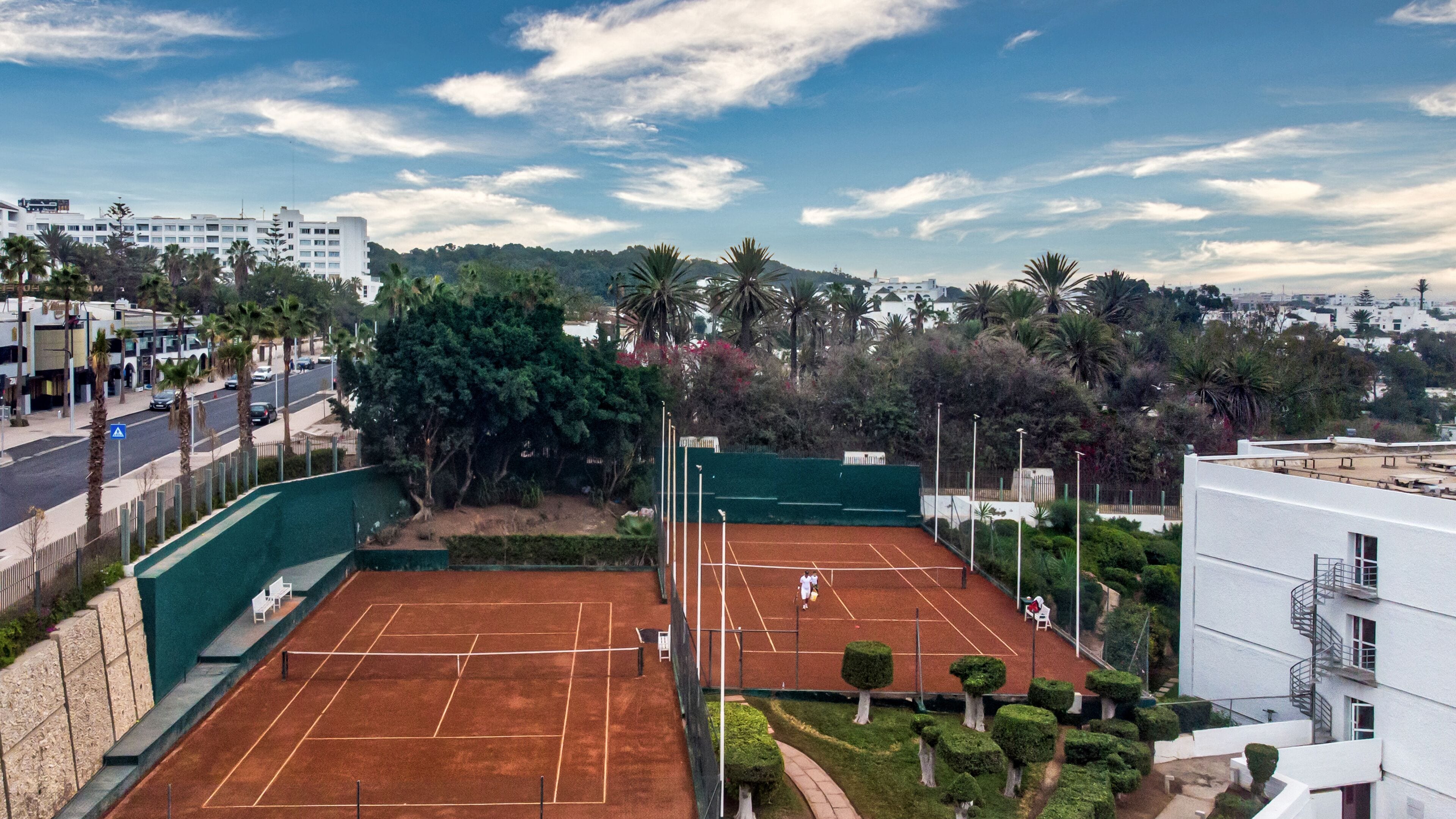 Un court de tennis entouré de verdure et de bâtiments.