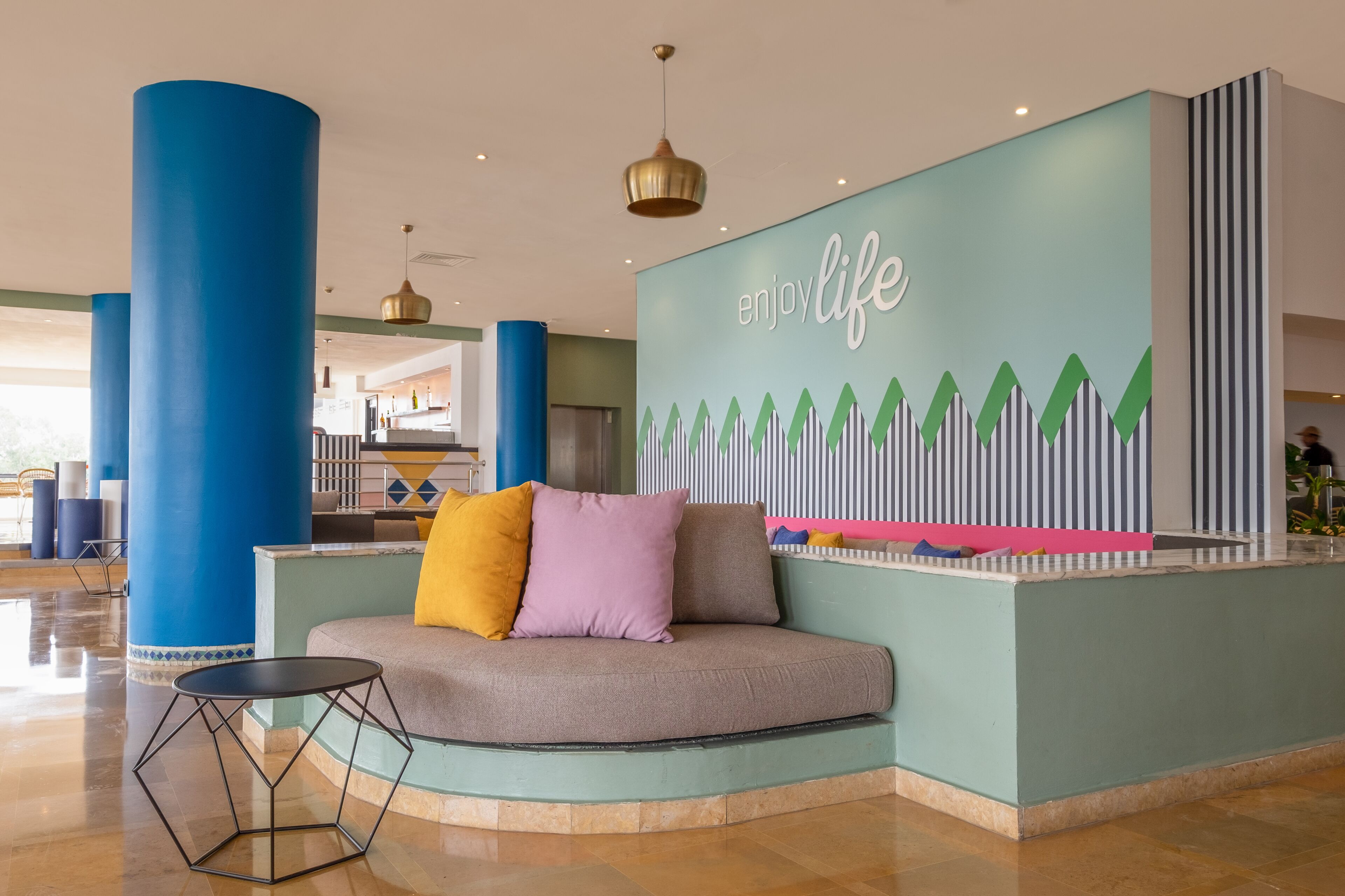 En lobby med en buet receptionsdisk, blå søjler og et muralmaleri med teksten 'Enjoy Life'.