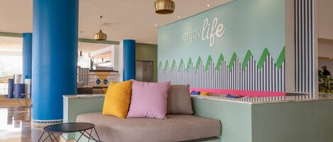 A lobby with a curved reception desk, blue pillars, and a 'Enjoy Life' mural.