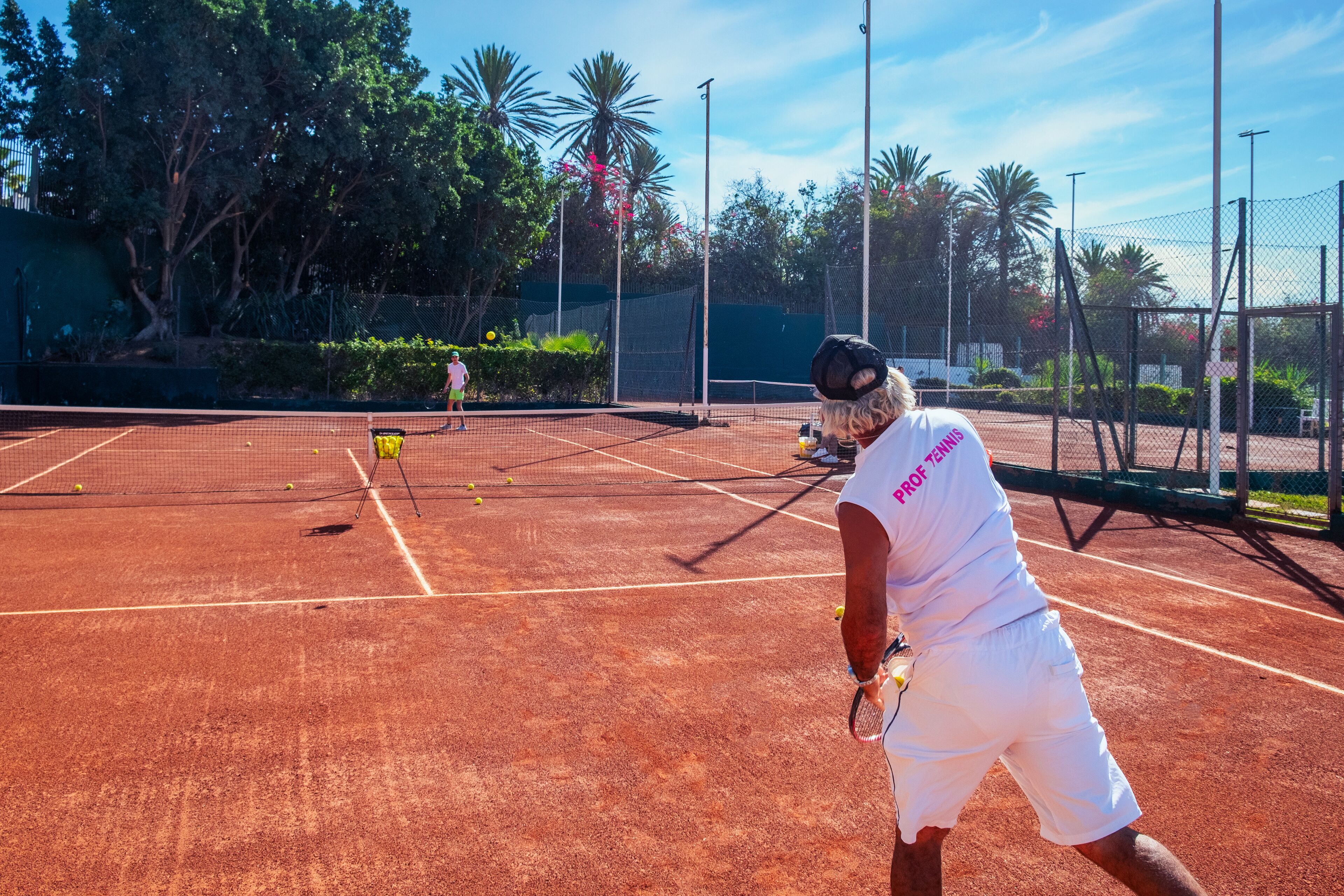 A tennis court with a net, surrounded by trees and a fence.