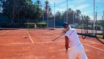 A tennis court with a net, surrounded by trees and a fence.