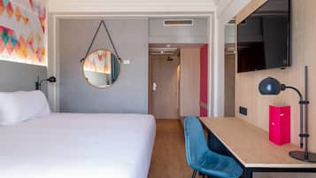 Una habitación de hotel con una cama grande, un escritorio con silla, un televisor montado en la pared y un espejo.
