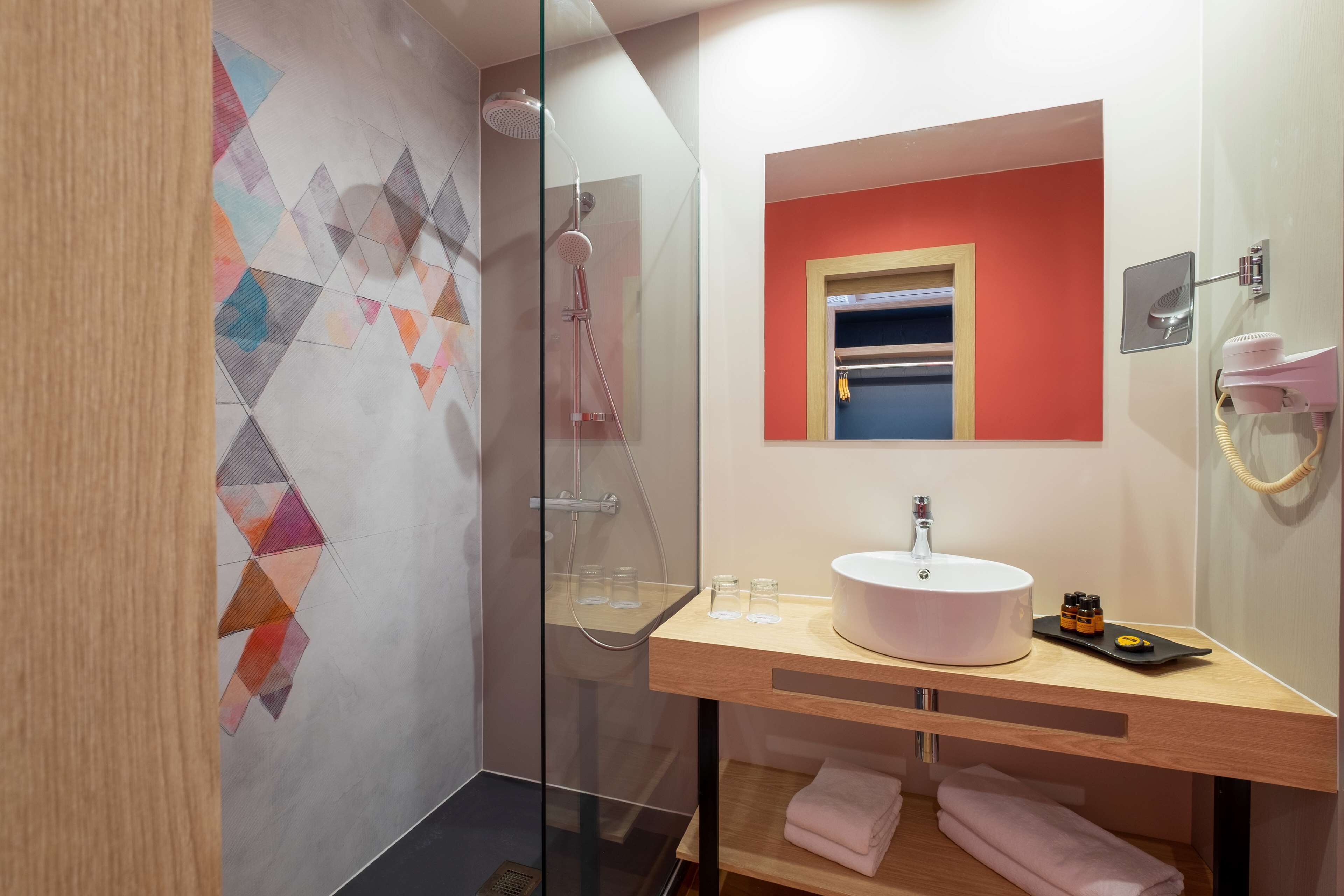 A modern bathroom with a glass-enclosed shower, a wooden vanity with a sink, and a mirror with a red accent wall.