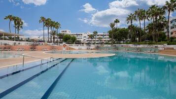 Una piscina con sillas de descanso, palmeras y un edificio al fondo.