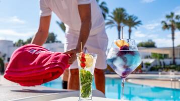 A poolside setting with a clear view of a swimming pool, a person in white attire, and two glasses of iced drinks with fruit garnishes.