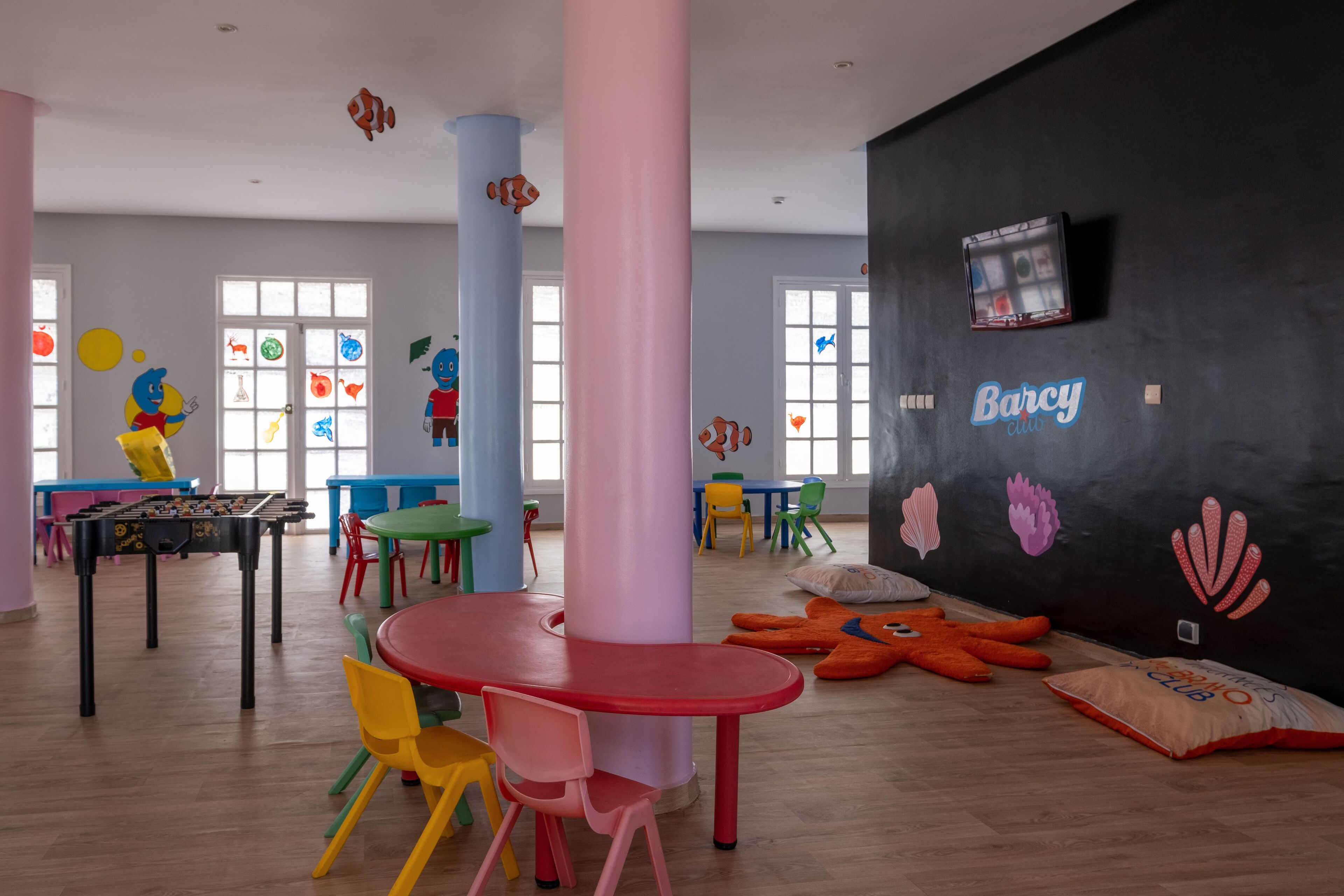Une salle de jeux pour enfants aux couleurs vives, avec des tables, des chaises et des décorations murales à vocation éducative.