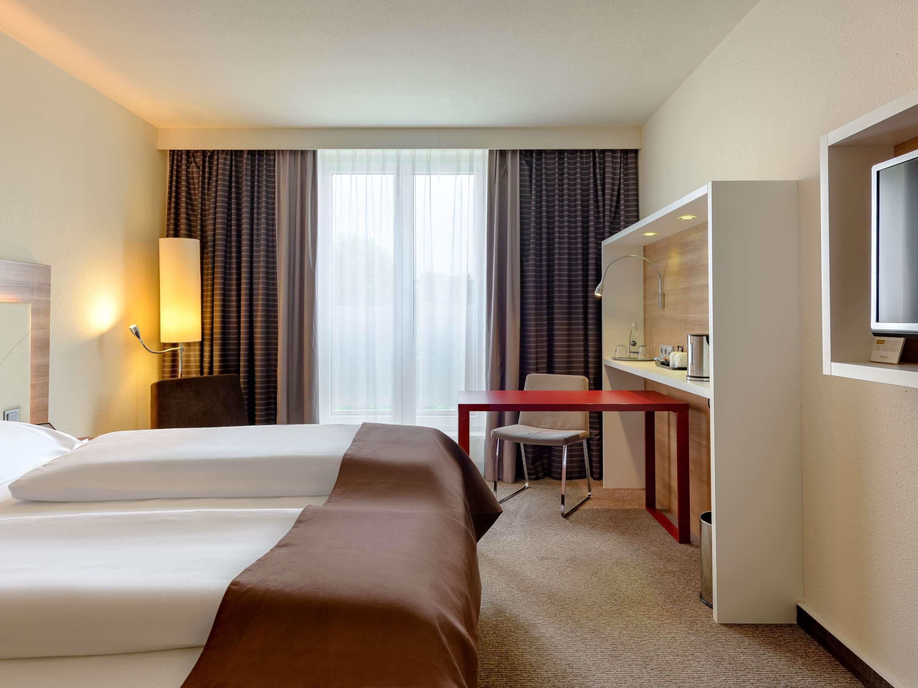 Una habitación de hotel con dos camas, un escritorio con silla, un televisor y una lámpara.