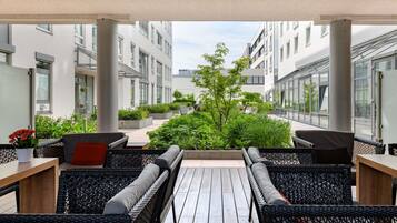 Un espacio al aire libre techado con mobiliario de mimbre, una terraza de madera y vistas a un complejo moderno de edificios.