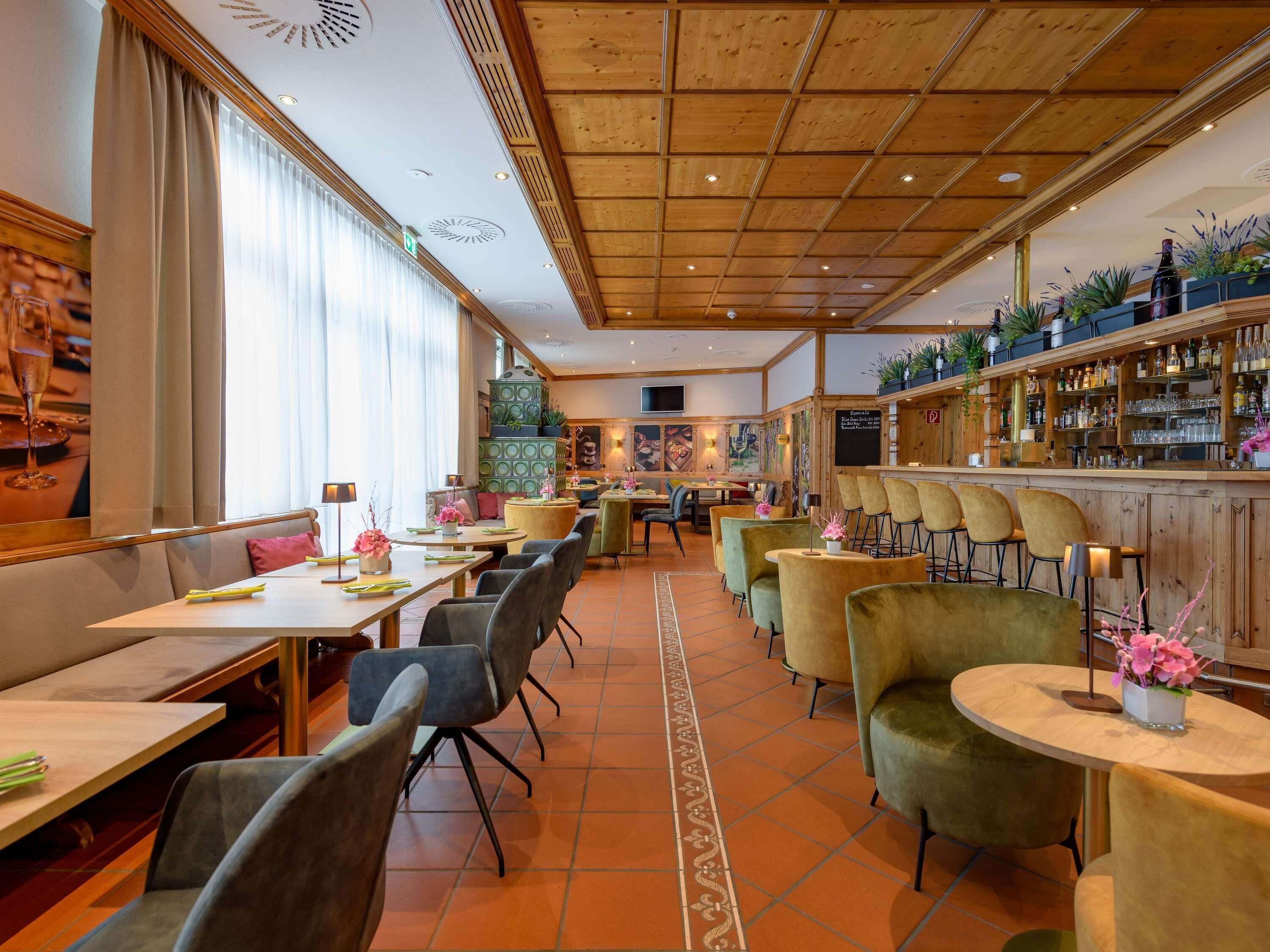 Un restaurante con techo de madera, varias mesas de comedor, sillas y una zona de bar con estantes llenos de botellas.