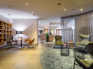 A modern hotel lobby with a round seating area, a bookshelf, and a reception desk. - Mercure Hotel Stuttgart Airport Messe (Stuttgart)