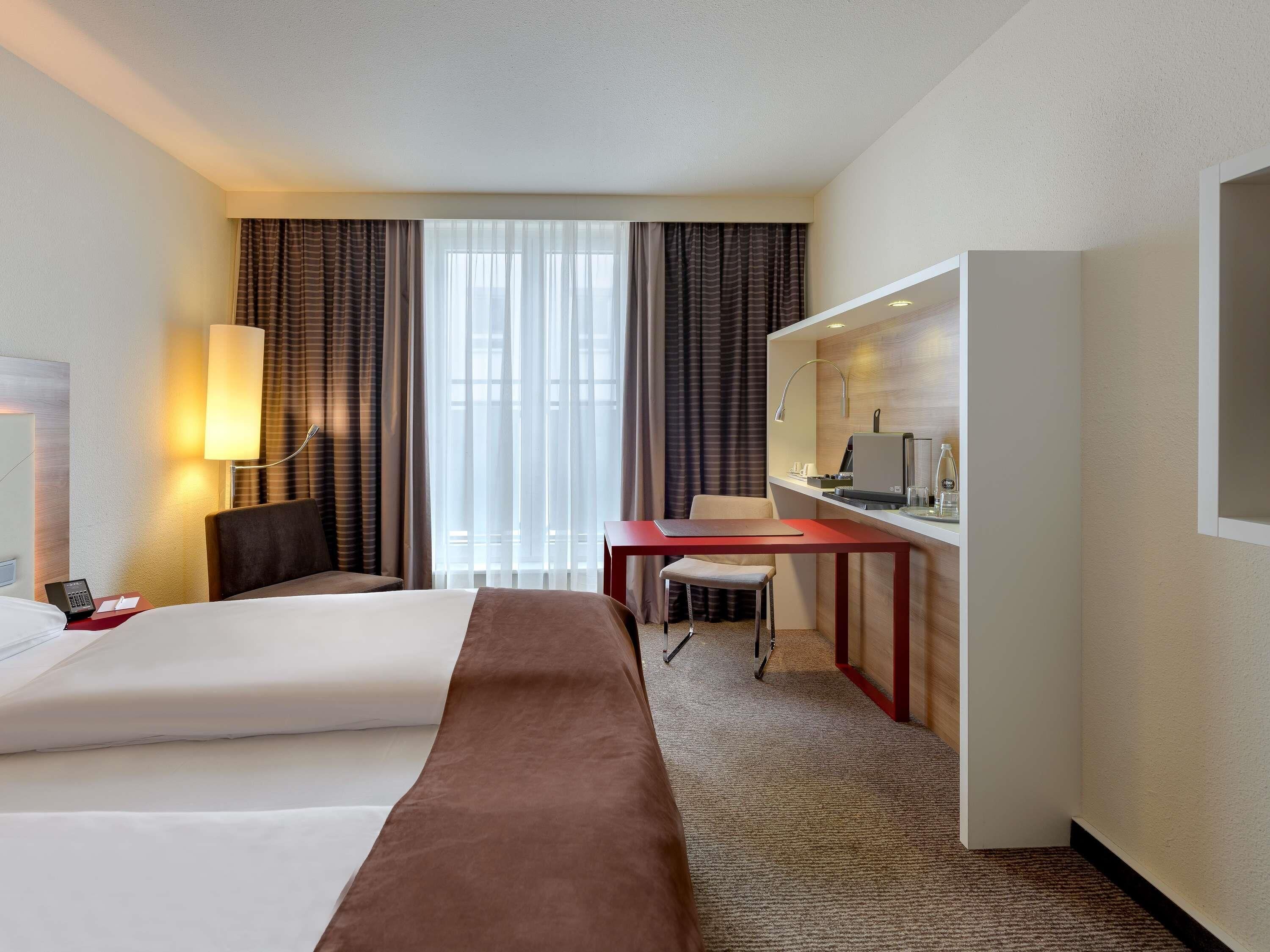 Une chambre d’hôtel équipée d’un lit, d’un bureau, d’une chaise, d’une lampe et offrant une vue sur l’extérieur.