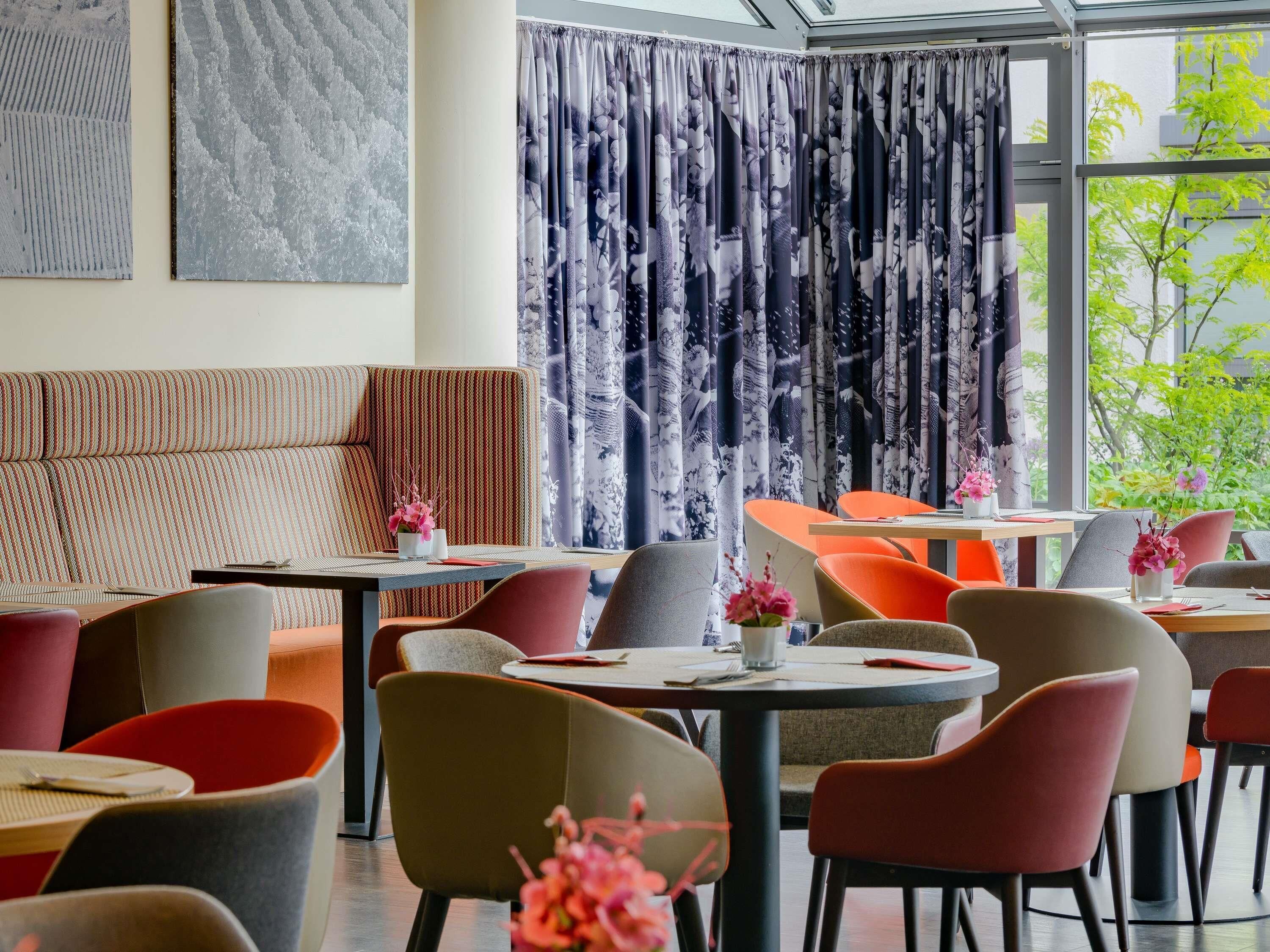 A modern restaurant interior with a mix of seating options, including booths and tables, and a large window with a view of greenery outside.