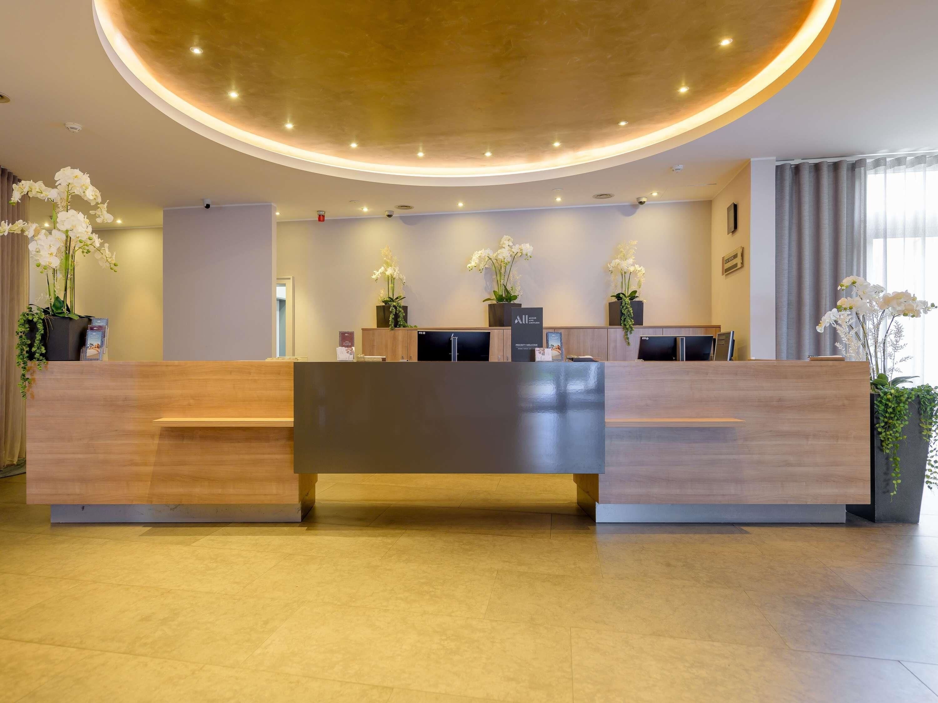 A modern reception desk with a wooden finish, a circular ceiling light fixture, and white orchids in vases.